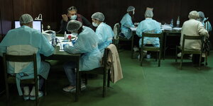 Medizinisches Personal in Schutzkleidung sitzt um Tische vor den Impfungen