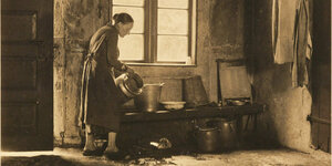 Eine Frau gießt in einem alten Bauernhaus eine Kanne aus.