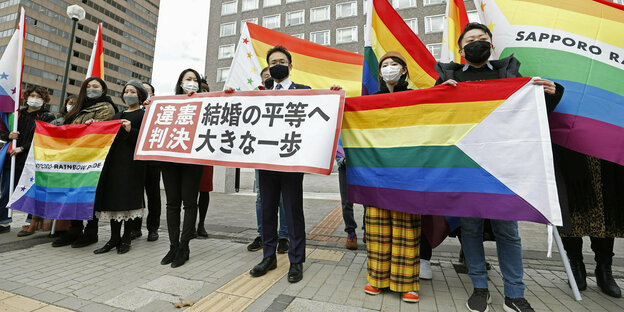 Anwälte der Kläger und Unterstützer halten Regenbogenflaggen und ein Transparent mit der Aufschrift: "Verfassungswidriges Urteil" vor dem Bezirksgericht Sapporo hoch