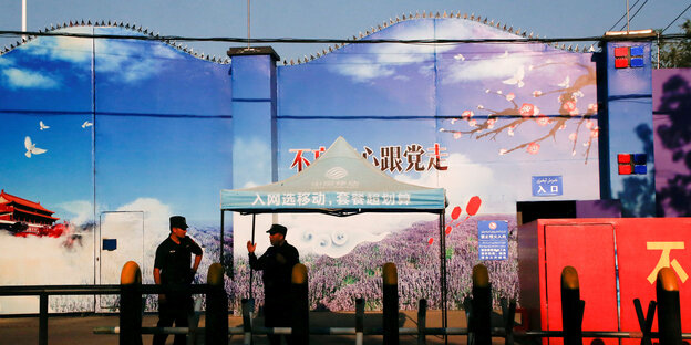 Zwei Sicherheitskräfte unterhalten sich vor der bunten Fassade eines Bildungszentrums in der chinesischen Provinz Xinjiang