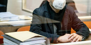 Ein Mann hinter einer Glasscheibe trägt eine FFP2-Maske auf der geschrieben steht: Keine Grundrechte