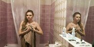 Filmszene: Frau in Handtuch gehüllt mit nassen Haaren in einem kleinen Bad, schaut verunsichert