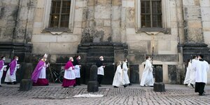 Bischof des Bistums Dresden-Meißen und Ministranten gehen über einen Platz neben einer Kirche und tragen Mund-Nasnschutz