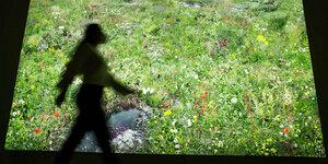 Eine Frau läuft vor Lichtinstallation die eine Blumenwiese zeigt