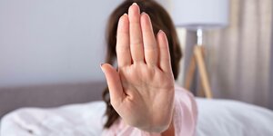 Eine Frau im Schlafzimmer macht Stopp-Zeichen mit der Hand