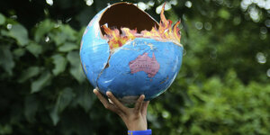 eine Han hält das Modell des brennenden Planeten Erde