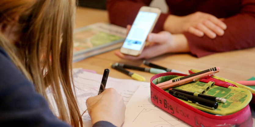 Kinder sitzen mit Smartphone am Schultisch