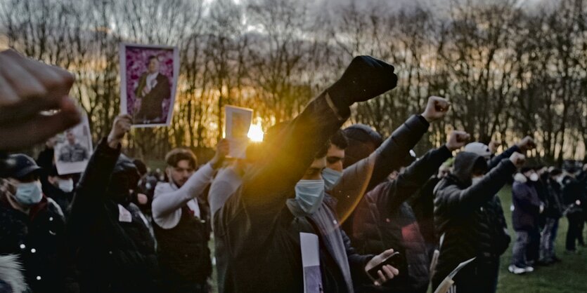 Junge Menschen in einem Park strecken den rechten Arm mit geschlossener Faus in die Luft.