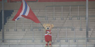 Maskottchen Paule steht einsam Fahne schwenkend auf der leeren Tribüne des Heidenheimer Stadions