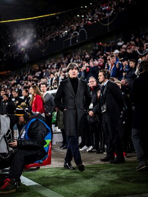 Jogi Löw in schwarzem Mantel läuft im Stadion zwischen den Zuschauern hindurch