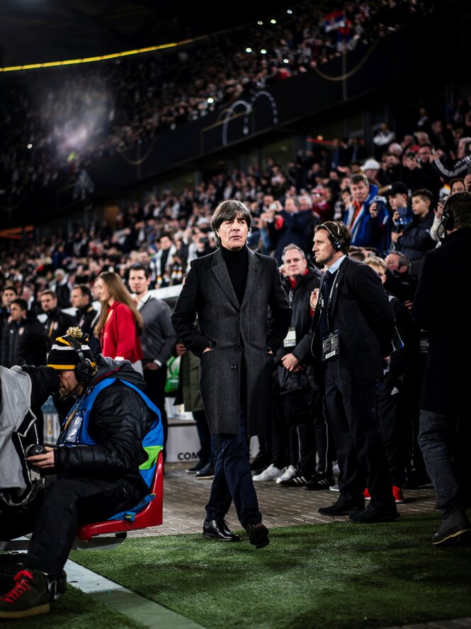 Jogi Löw in schwarzem Mantel läuft im Stadion zwischen den Zuschauern hindurch