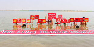 Mehrere Menschen fast untergetaucht im braunen Wasser eines Flusses. Sie halten Plakate gegen den Militärputsch in Myanmar hoch