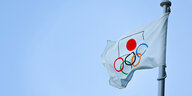 Japanische Flagge mit Olympia-Ringen weht am Mast vor blauem Himmel