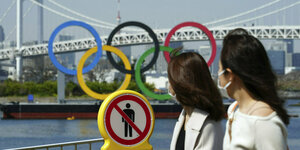 Zwei Japanerinnen schauen auf die olympischen Ringe und ein Verbotsschild.