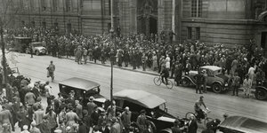 Vor dem Kriminalge-richt Moabit warten 1931 Hunderte Schaulustige auf die Ankunft der Zeugen im Edenpalast-Prozess, darunter der Zeuge Adolf Hitler. Zu sehen sind gut behütete Männerund Frauen in langen Staubmänterln
