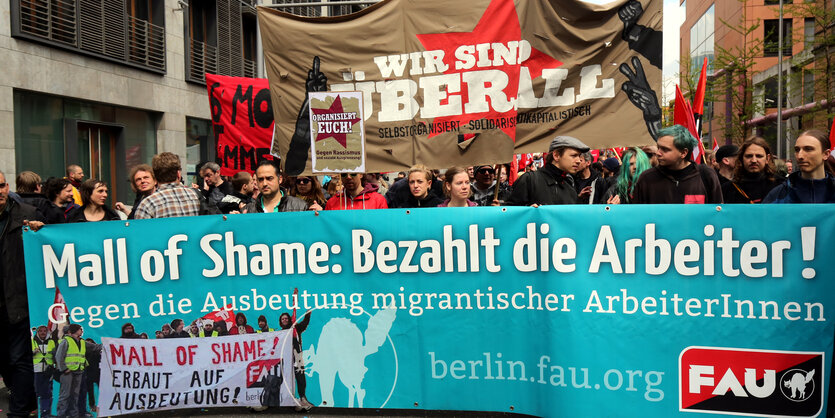 Menschen stehen hinter einem Banner, das die Bezahlung der Arbeiter fordert