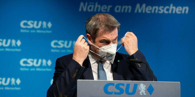 Markus Söder setzt sich eine Mundschutzmaske auf
