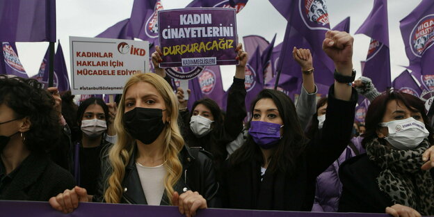 Frauen mit Masken auf einer Demonstration halten Schilder hoch und recken die Faust in die Luft