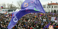 Menschenmenge demonstriert, lila Fahne im Vordergrund