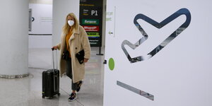 Eine Frau mit Mund-Nasenschutz und Rollkoffer in einem Flughafen auf Mallorca