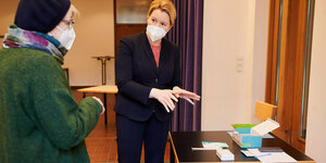 Familienministerin Giffey steht mit Mund-Nasen-Schutz in einer Kita und prüft Test für Kita-Kinder