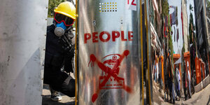 Ein Demonstrant traegt gelben Helm und Gasmaske und ein silbenes Schutz-Schild mit durchgestrichenen Foto des Generals Min Aung Hlaing sowie der Aufschrift "People"