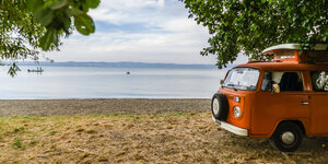 Ein Campingbus Volkswagen VW Bulli T2 steht unter Bäumen in der Landschaft an einem Seeufer, Bolsena, Latium, Italien