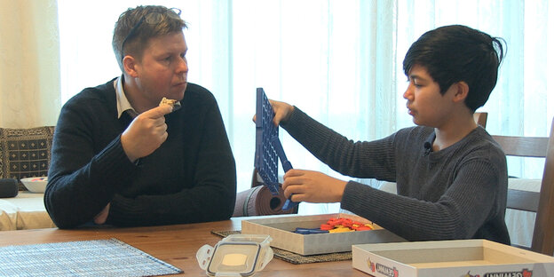 Ein Mann und ein Junge sitzen mit einem Brettspiel am Tisch Ein Mann und ein Junge sitzen mit einem Brettspiel am Tisch
