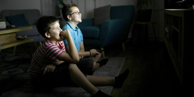 Zwei Kinder, vermutlich Jungs, schauen im Dunkeln fern
