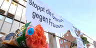 Blumen und Grablichter stehen unter einem Banner mit der Aufschrift "Stoppt Gewalt gegen Frauen"