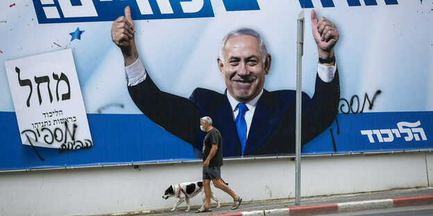 Benjamin Netanyahu auf einem großen Wahlplakat - dacor läuft ein älterer Herr und schiebt sein Fahrrad