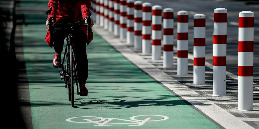 Eine Frau fährt auf einem Radweg, der mit rot-weißen Pollern abgegrenzt ist