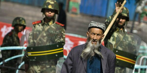 Langbärtiger uigurischer Mann vor Bereitschaftspolizisten