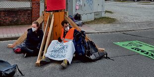 Klimaschützer mit Masken und einem Transparent sitzen an eine Straßensperre gelehnt.