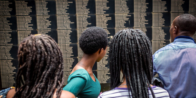 Besucher lesen an einer Wand mit Namen von Ermordeten