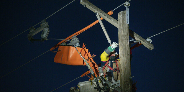 Das Bild zeigt einen Menschen in Sicherheitskleidung, der nachts an einem Strommast schraubt.