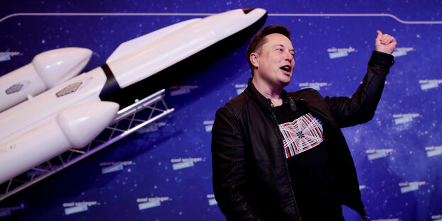 Elon Musk gestikuliert vor einem Rakten-Modell