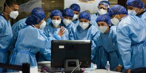 Medizinisches Personal mit Schutzkleidung blickt auf einen Monitor