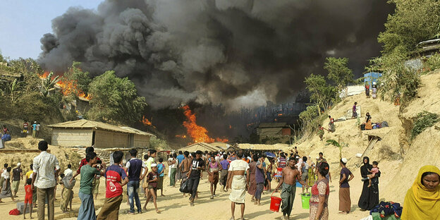 Rauch und Flammen steigt nach einem Brand im Rohingya-Flüchtlingslager in Balukhali auf - Menschen beobachten den Brand und tragen ihre Habseeligkeiten weg