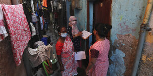 Zwei Frauen mit Mund-Nasenschutz und Fragebogen unterhalten sich mit einer Frau in einer Gasse in Mumbai