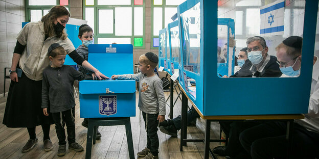 23.03.2021, Israel, Jerusalem: Eine orthodoxe Jüdin gibt mit ihren Kindern ihre Stimme für die israelischen Parlamentswahlen in einem Wahllokal ab.
