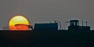 Ein Landwirt bringt während eines Sonnenuntergangs Gülle auf einem Feld aus.