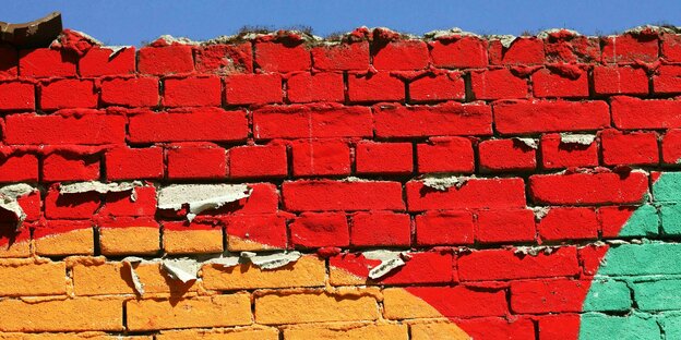 Bunt bemalte Ziegelsteinmauer, in den Farben Rot, Orange und Grün.