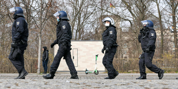 Vier Polizist:innen laufen hintereinander in Demonstrationsausrüstung durch das Regierungsviertel