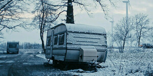 Ein Wohnwagen steht auf einem Grundstück von einzelnen Bäumen umgeben. Es liegt Schnee