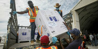 Männer laden große Kisten mit der Aufschrift "Covax" von einem Lastwagen