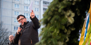 Michael Grunst, der Bürgermeister des Berliner Bezirks Lichtenberg, hat ein rundes Gesicht und kurze dunkelbraune Haare. Er trägt auf dem Foto eine schwarze Steppjacke und eine schwarze Brille. Grunst gehört der Linkspartei an und ist 51 Jahre alt.