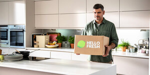 Ein Mann steht mit einer Hello Fresh Kiste in einer Küche