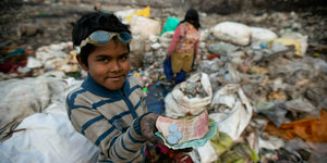 Ein Junge auf einer Müllhalde, er hält Geld in die Kamera