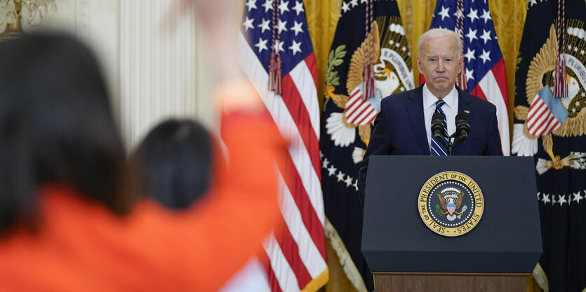 Biden an einem Rednerpult, im Vodergrund hebt eine Person ihren rechten Arm